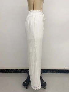 Dettaglio dei pantaloni plissettati bianchi a gamba larga con bordo in pizzo