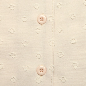 Detail von beigem Swiss-Dot-Stoff und zwei passenden Vierloch-Resin-Knöpfen