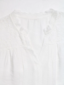 Detailed close-up of white v-neck shirt featuring floral lace patches and pleated texture