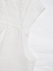 Detail of white sleeveless top featuring floral lace patchwork and textured woven fabric
