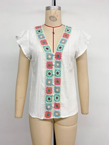 Detail of V-neck white blouse with colorful crochet floral patches and ruffled sleeves