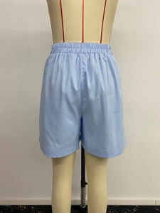 Dettaglio dei pantaloncini azzurri a vita alta con fascia elastica plissettata