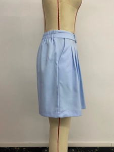 Dettaglio dei pantaloncini azzurri a vita alta con tasche laterali e design a pieghe