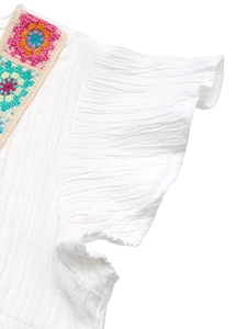 Detail of white crinkle fabric top with colorful bohemian crochet stitching and ruffle sleeves