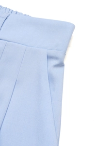 Dettaglio degli shorts a pieghe azzurri con vita elastica e trama in tessuto twill
