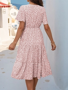 Pink polka dot summer dress featuring short sleeves and a tiered skirt on a sunlit street