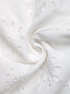 Detailed macro view of white eyelet lace fabric with intricate floral embroidery