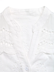 Detail of white V-neck blouse featuring intricate eyelet embroidery and scalloped edges