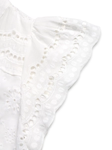 Detailed view of white cotton top featuring intricate floral eyelet embroidery and scalloped edges