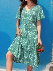 Detail of green V-neck dress with white floral print, cinched waist, and layered skirt