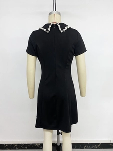 Detail view of the back of a black mini dress featuring a zipper and pearl collar