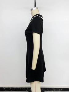 Detail view of a black short-sleeved dress featuring elegant white pearl bead trim at neckline