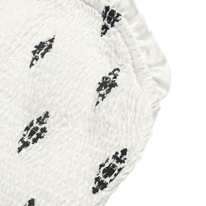 Detailed view of white smocked fabric with black diamond prints and ruffled edges