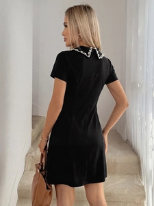 Detail of elegant white pearl beadwork on the neckline of a black short sleeve dress