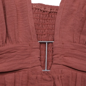 Detail of rust red cotton linen dress with metallic buckle and elastic smocked texture
