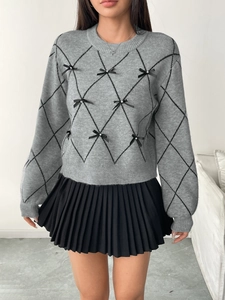 Detail of grey diamond-pattern knit sweater with delicate black bows and pleated skirt