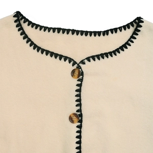Detailed macro view of beige fleece fabric with black embroidery and amber buttons