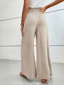 Detail of high-waist elastic pleats and draped khaki wide-leg trousers on model