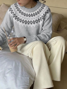 Detail of grey Fair Isle knit sweater and white corduroy pants in a cozy indoor setting