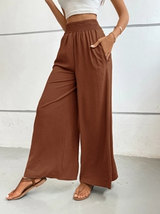 Detail view of brown high-waisted wide-leg trousers with elastic waistband and side pockets