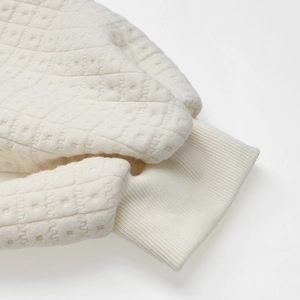 Detailed view of the ribbed cuffs and textured diamond pattern on the beige sweatshirt