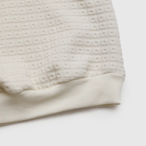 Macro view of cream-colored thick textured fabric with ribbed hem detail and quilted pattern