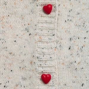 Close-up of cream knit fabric with color flecks and vivid red heart-shaped buttons