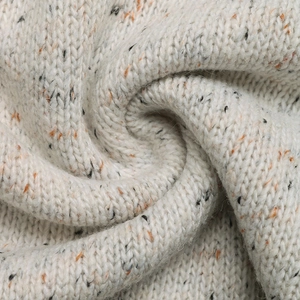 Close-up of beige knit fabric with orange and black flecks showing soft texture