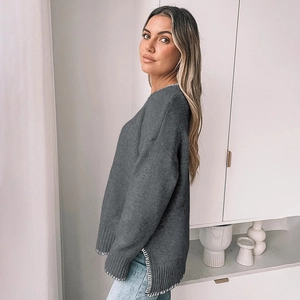 Detail of loose fit grey knit sweater featuring white contrast stitching and side slits