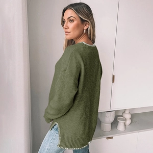 Detail of dark green knit sweater featuring white contrast stitching on the side slit hem