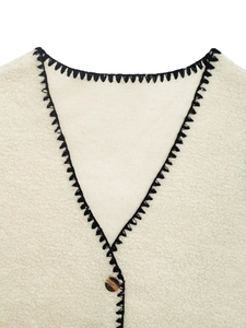 Dettaglio macro dello scollo a V con cuciture a contrasto e bottone marrone sul gilet crema