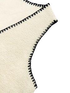 Dettaglio ravvicinato di un gilet in pile bianco con cucitura a sopraggitto nera