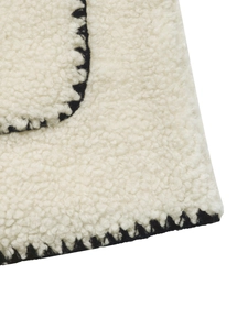 Dettaglio del tessuto in pile crema con bordi decorativi cuciti a mano in nero