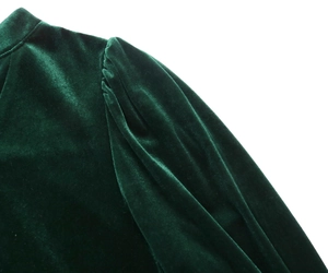 Detail view of dark green velvet dress showing shoulder pleats and premium fabric texture