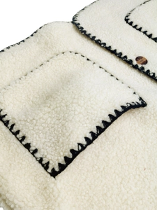Dettaglio del gilet in pile bianco con cuciture a contrasto nere e bottone in resina