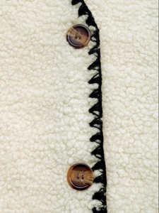 Dettaglio di gilet in pelliccia crema con bottoni marmorizzati e bordi a zigzag neri