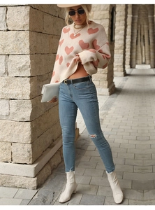 Outdoor street shot of a beige knit sweater with pink hearts and ripped denim jeans