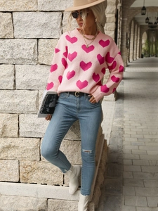 Close-up of pink knit sweater with jacquard hearts and distressed denim jeans