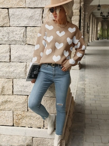 Detail of a camel knit sweater featuring a white heart pattern and ribbed crew neck finish