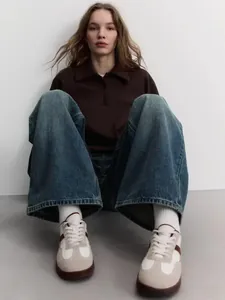 Detail of a brown long sleeve polo shirt paired with wide-leg denim jeans and sneakers