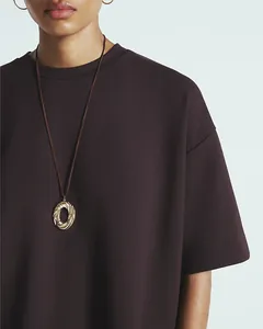 Close-up of a minimalist gold twisted round pendant on a dark brown woven cord necklace