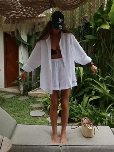 Detail of white linen shirt and high-waist shorts set for women in outdoor resort setting