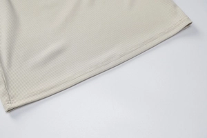 Dettaglio della maglia a costine crema con cuciture precise a doppio ago sull'orlo