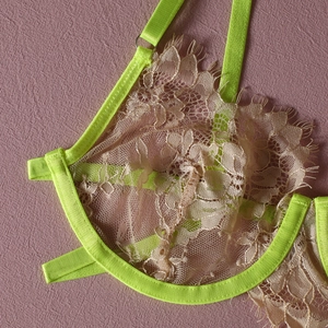 Close-up of skin-tone lace lingerie with neon green trim and floral eyelash lace details