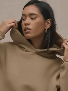 Close-up of premium camel hoodie fabric with thick knit texture and minimalist golden earrings
