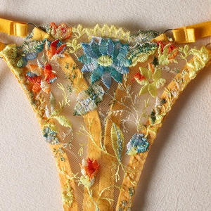 Detailed close-up of vibrant floral embroidery on sheer yellow lace lingerie panty