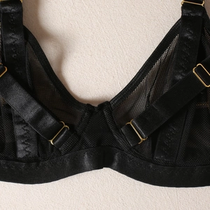 Close-up of black mesh bra with satin straps and gold metal adjustment buckles