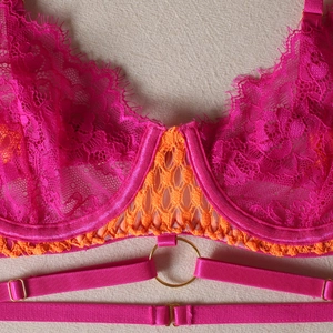Detailed macro shot of fuchsia lace bra with orange mesh trim and gold hardware rings