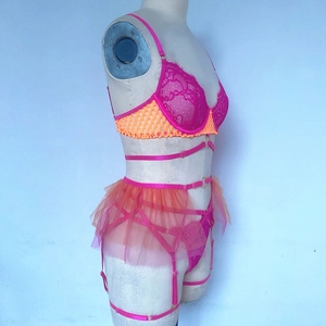 Detailed side view of hot pink lace bra and orange mesh skirted garter on mannequin