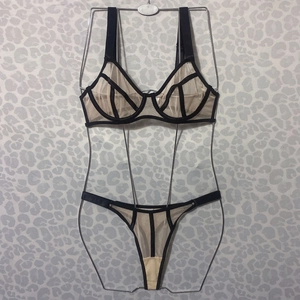 Detail of sheer black lace and pink mesh lingerie set displayed on a metal frame